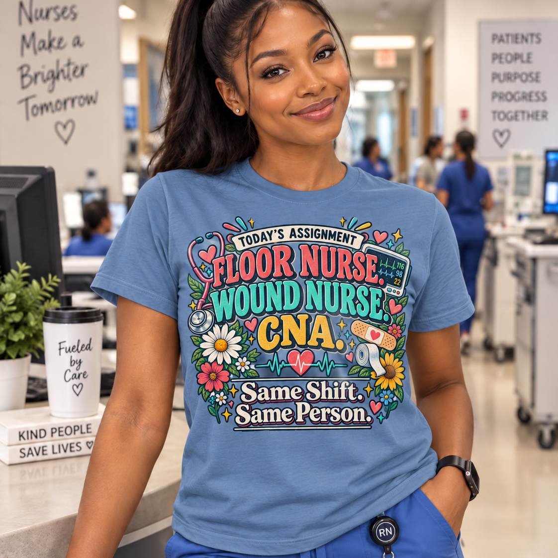 A woman in a hospital setting wearing a blue graphic t-shirt that reads 'TODAY'S ASSIGNMENT FLOOR NURSE WOUND NURSE CNA Same Shift Same Person' with colorful floral and medical-themed illustrations. She is also wearing blue scrubs and an RN badge.