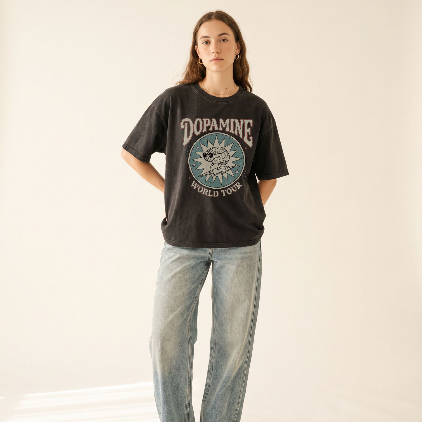 A woman modeling a dark charcoal graphic t-shirt with 'DOPAMINE WORLD TOUR' and a circular dog print, paired with light-wash wide-leg jeans against a plain off-white background.