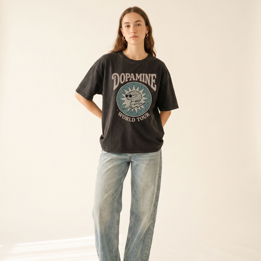 A woman modeling a dark charcoal graphic t-shirt with 'DOPAMINE WORLD TOUR' and a circular dog print, paired with light-wash wide-leg jeans against a plain off-white background.