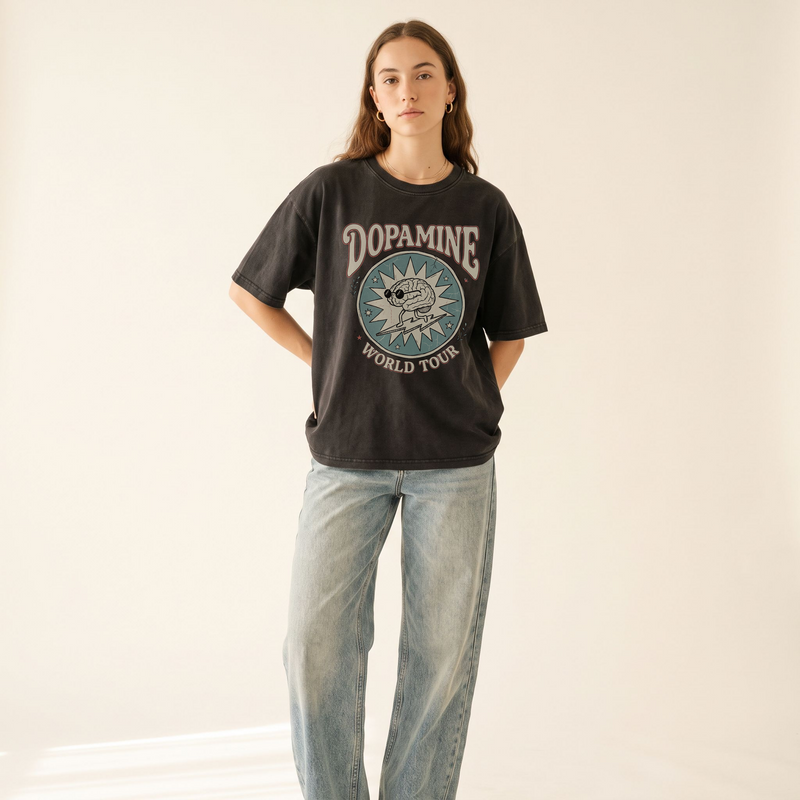 A woman modeling a dark charcoal graphic t-shirt with 'DOPAMINE WORLD TOUR' and a circular dog print, paired with light-wash wide-leg jeans against a plain off-white background.