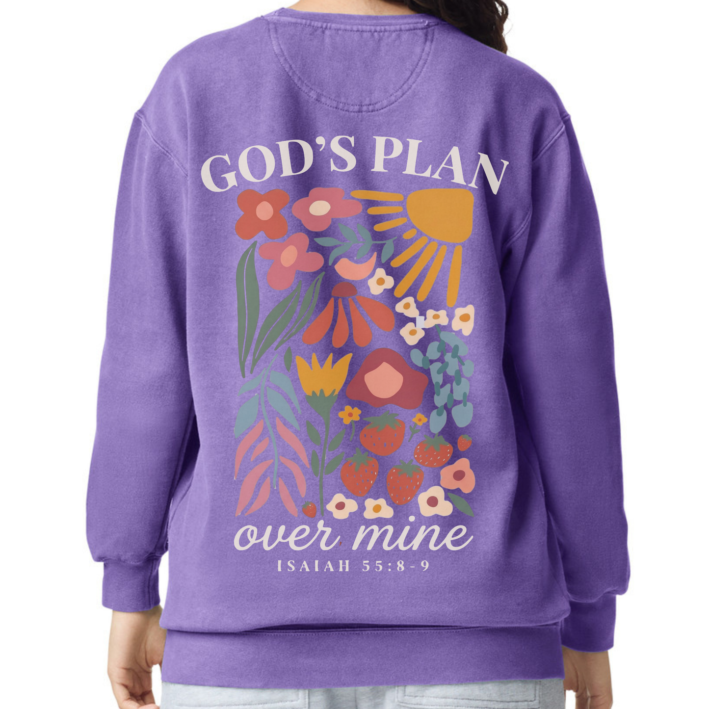 A person wearing a purple crewneck sweatshirt, shown from the back. The sweatshirt features a colorful graphic of flowers, a sun, and hearts, with the text 'GOD'S PLAN over mine ISAIAH 55:8-9' printed on it.