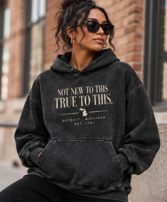 Woman wearing oversized black Detroit hoodie with Not New to This True to This graphic and vintage acid wash finish